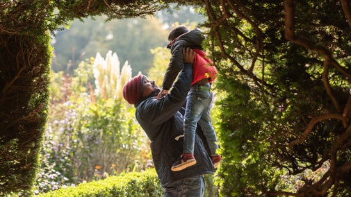 Man holding a child up in the air as they both smile, in the grounds at Powis Castle, Powys